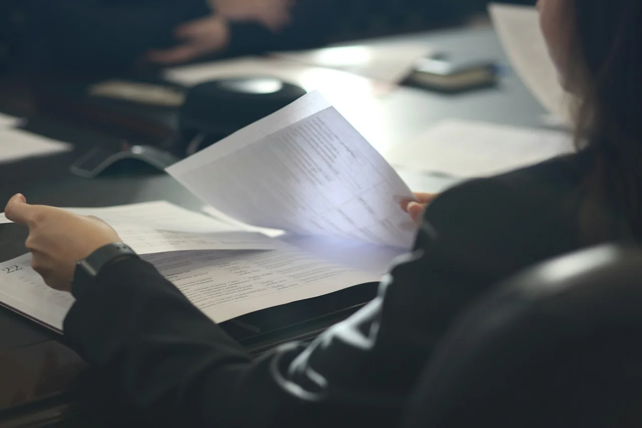 A woman in a business suit is focused on reading documents at a desk.