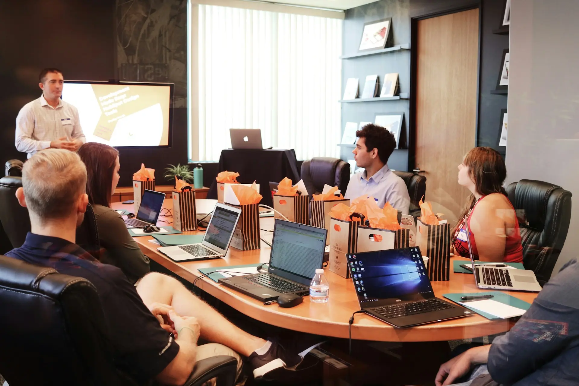 A group of diverse individuals seated at a table, each using a laptop, engaged in discussion or collaboration.