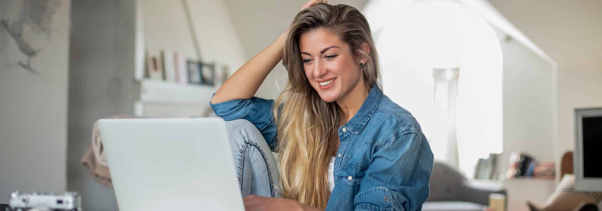 A woman smiles while seated on a couch, working on her laptop, exuding a sense of joy and productivity.