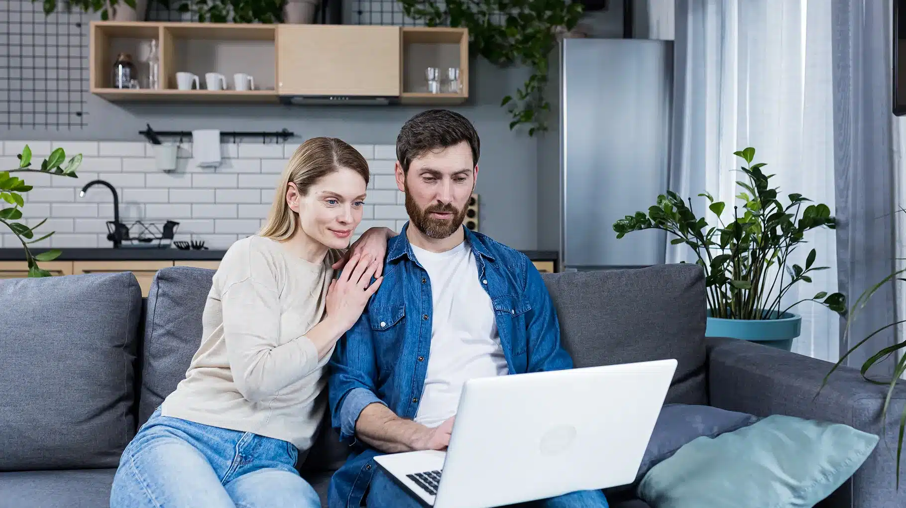 A man and woman sitting together on a couch, focused on a laptop placed on their laps.
