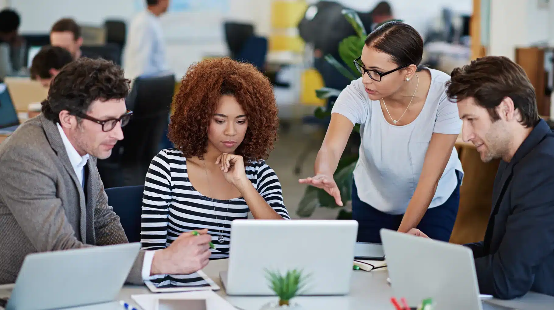 A diverse group of professionals collaborating on laptops in a modern office environment.