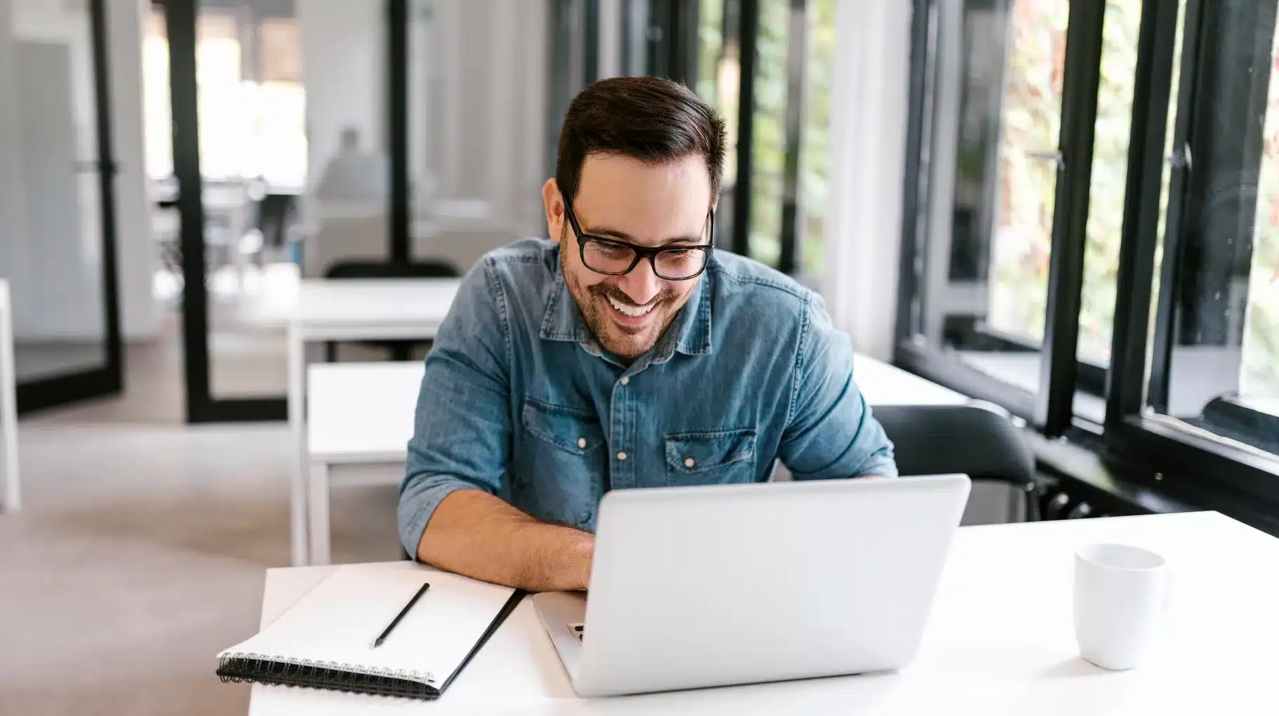A smiling man wearing glasses is using a laptop, engaged in his work or leisure activity.