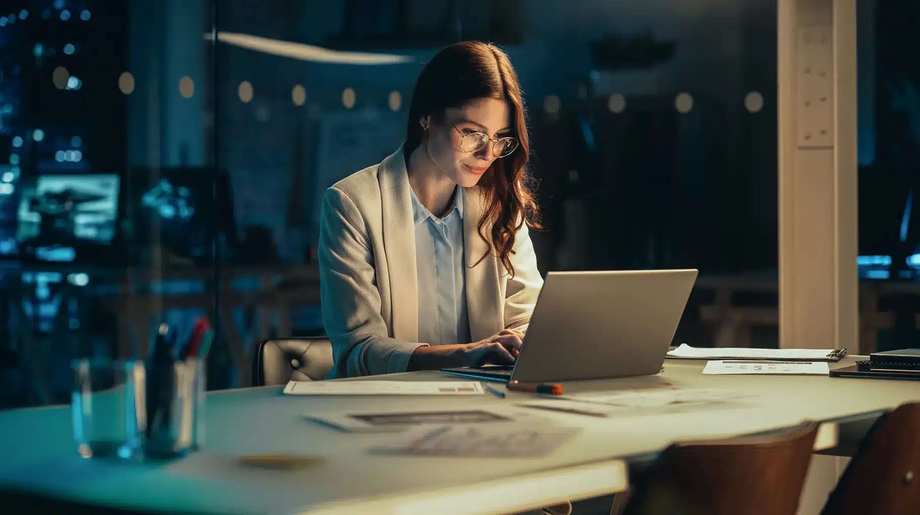 A woman sits at a table, focused on her laptop, with a calm expression in a well-lit indoor setting.