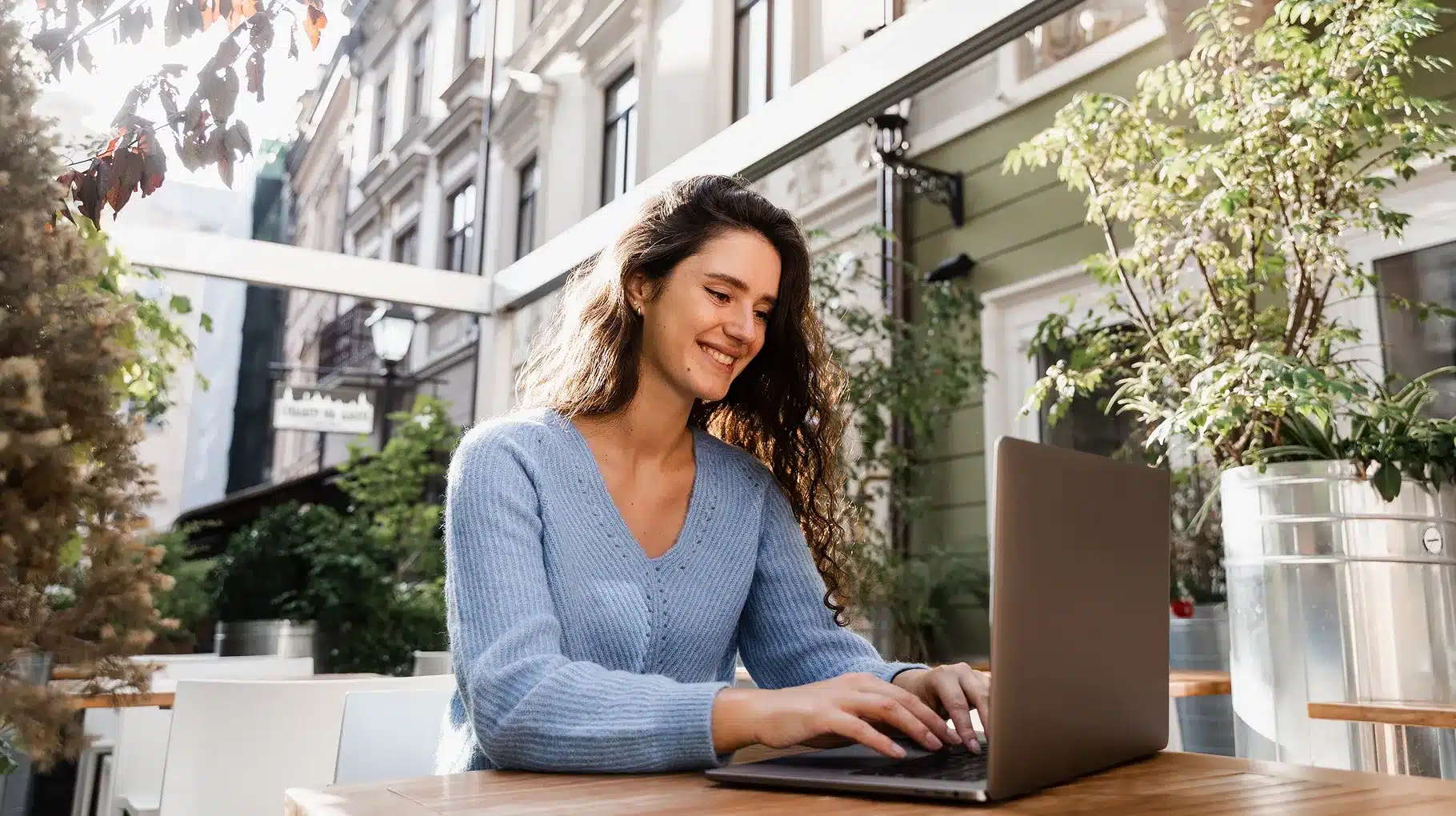 A woman sitting at a table, focused on her laptop, with a calm expression and a cozy environment around her.