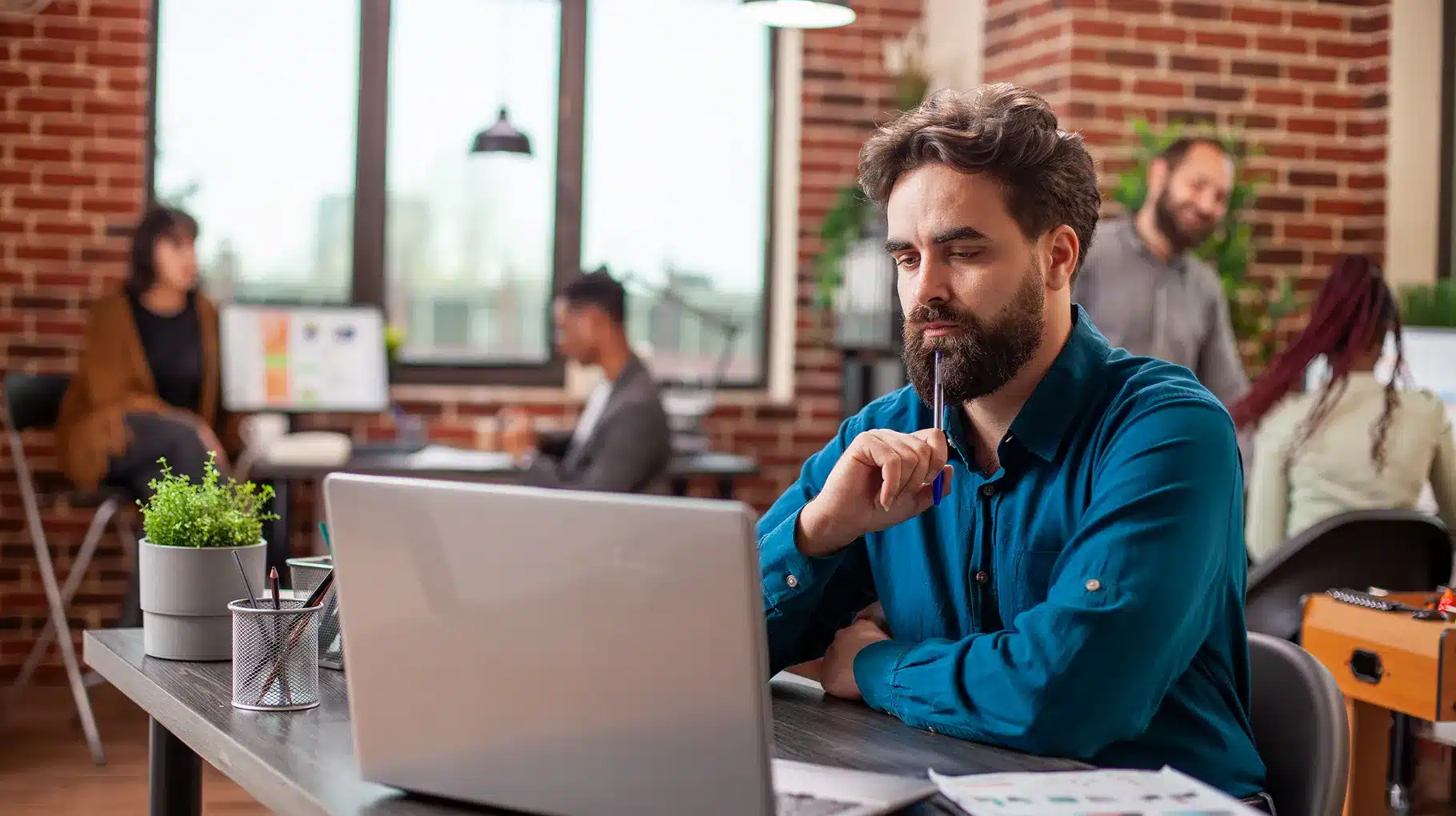 A man sitting at a desk, focused on his laptop, with a notepad and pen beside him.