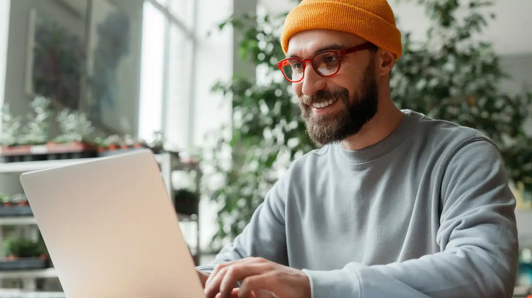 A bearded man wearing glasses is focused on using a laptop at a desk.