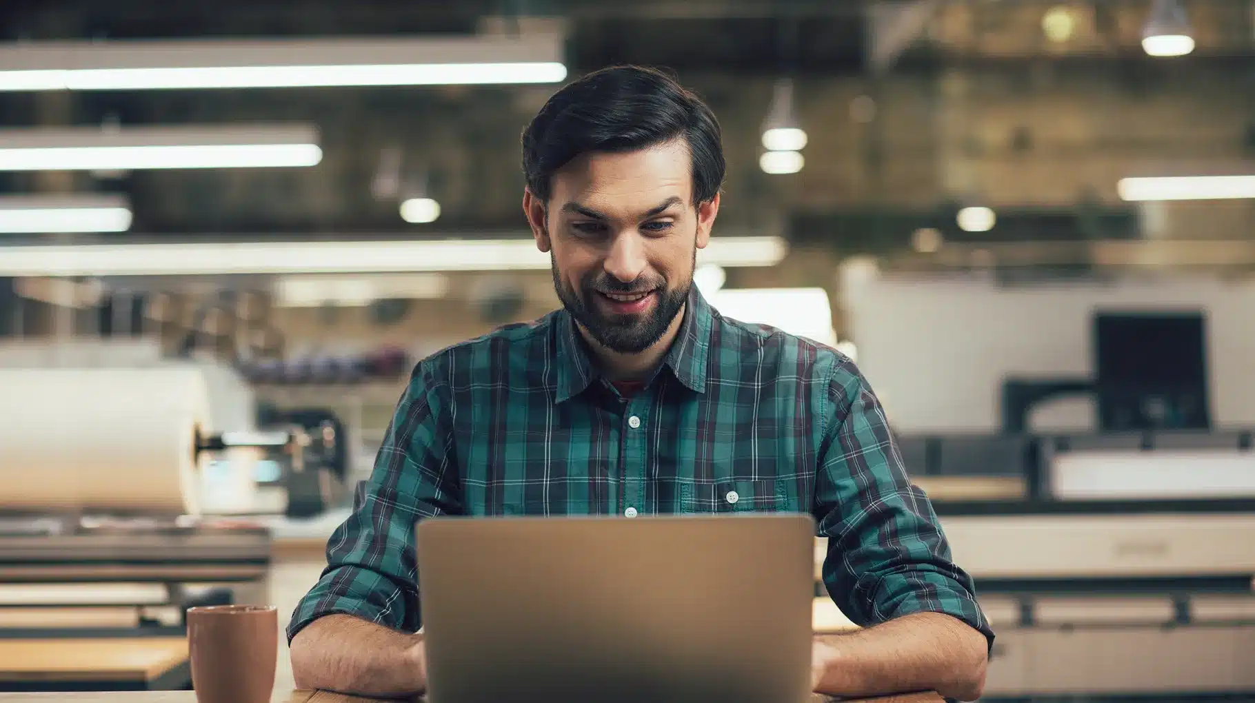 A man smiles while using a laptop, engaged in work or leisure on a bright, cheerful day.