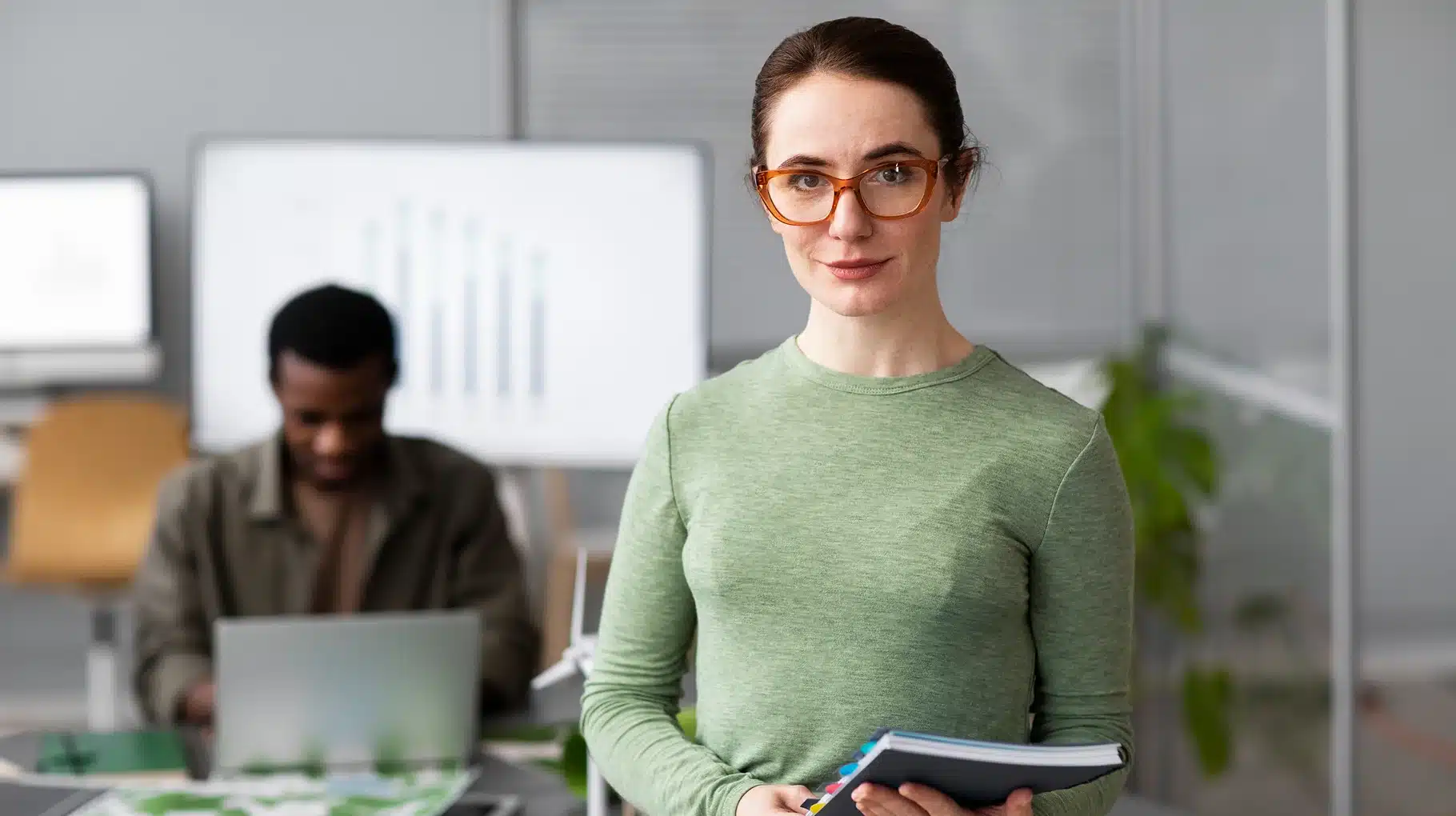 A woman with glasses stands in front of a laptop, focused on her work.