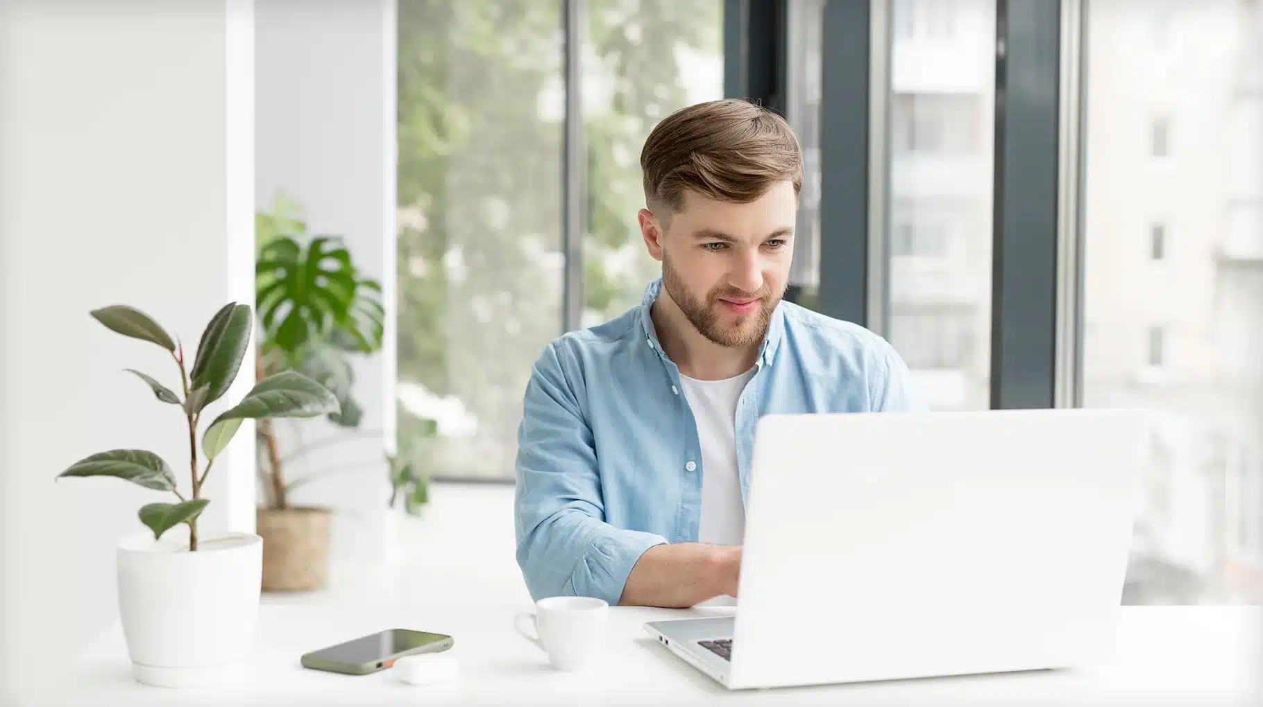 A man sitting at a desk, focused on his laptop, with a notepad and pen beside him.
