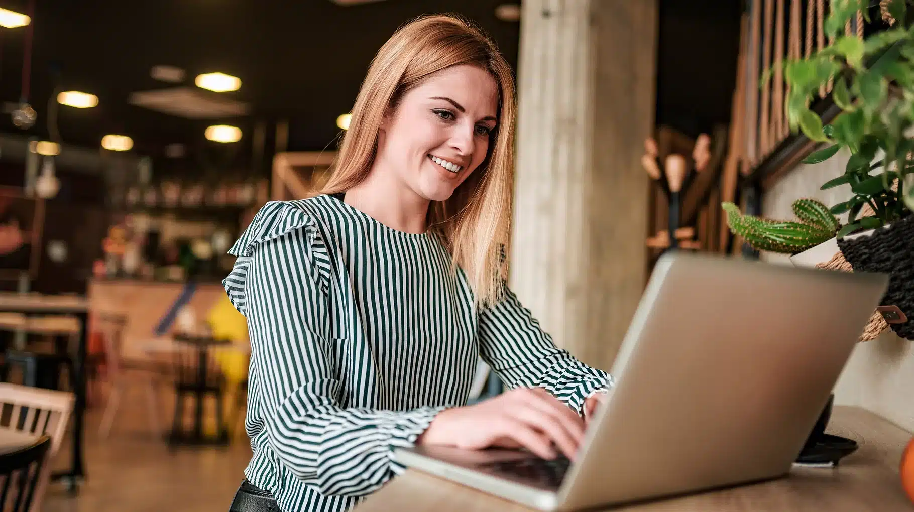 A woman smiles while working on her laptop, conveying a sense of joy and engagement in her task.