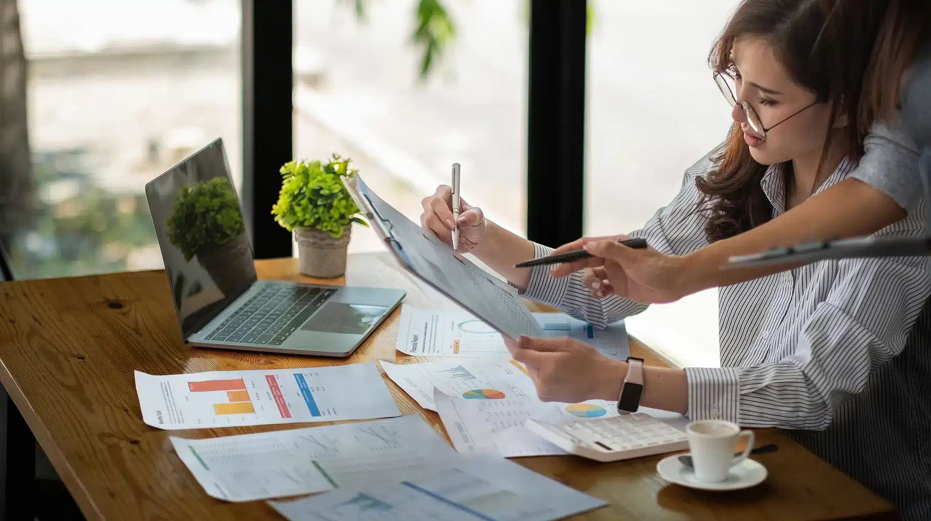 Two women collaborating on paperwork at a table, focused on their tasks in a professional setting.