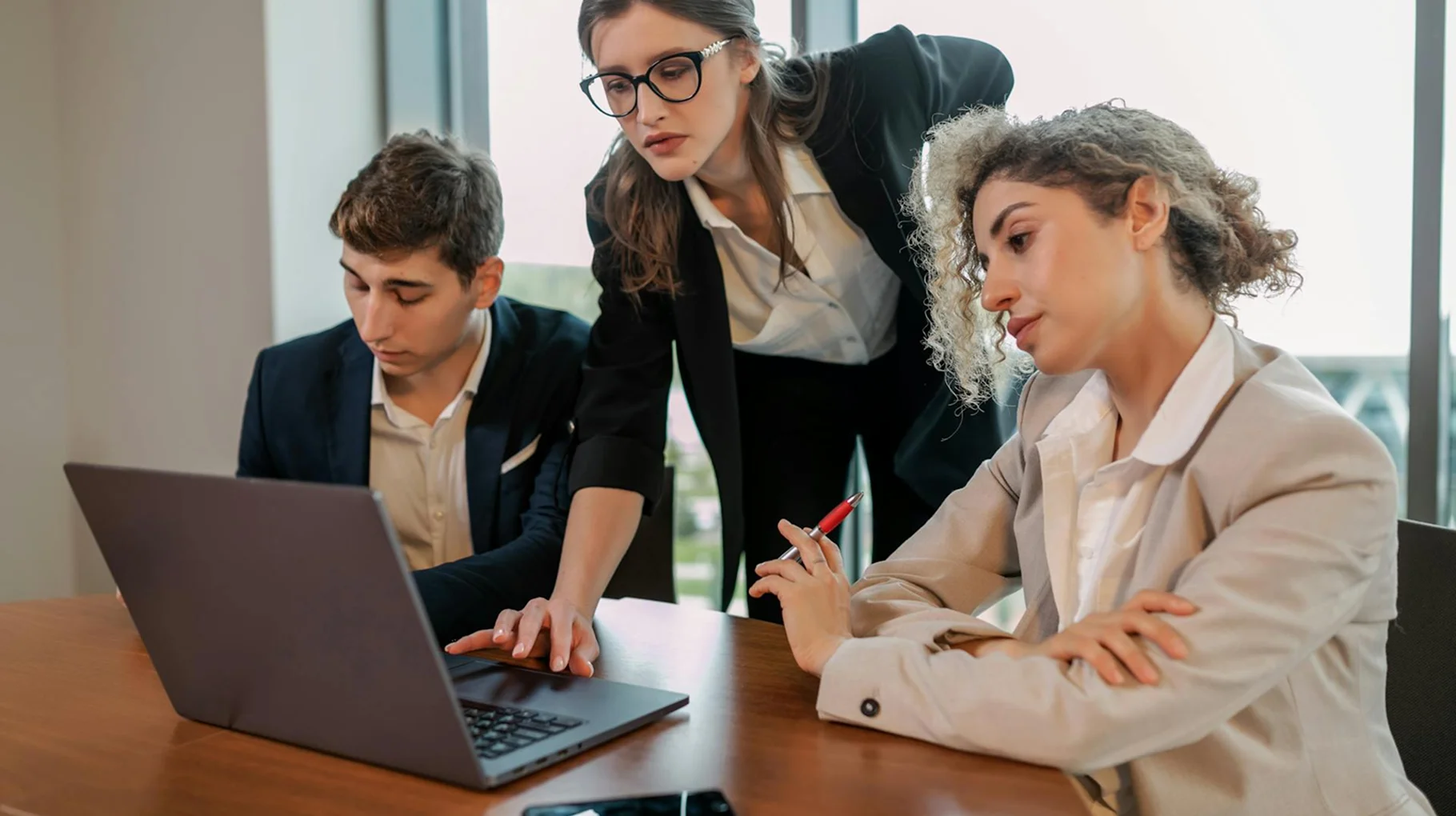 A group of three colleagues engaged in a discussion while working on a laptop together.