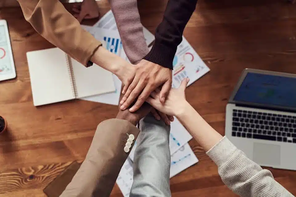 Business professionals stacking hands together over a conference table, symbolizing teamwork and collaboration.