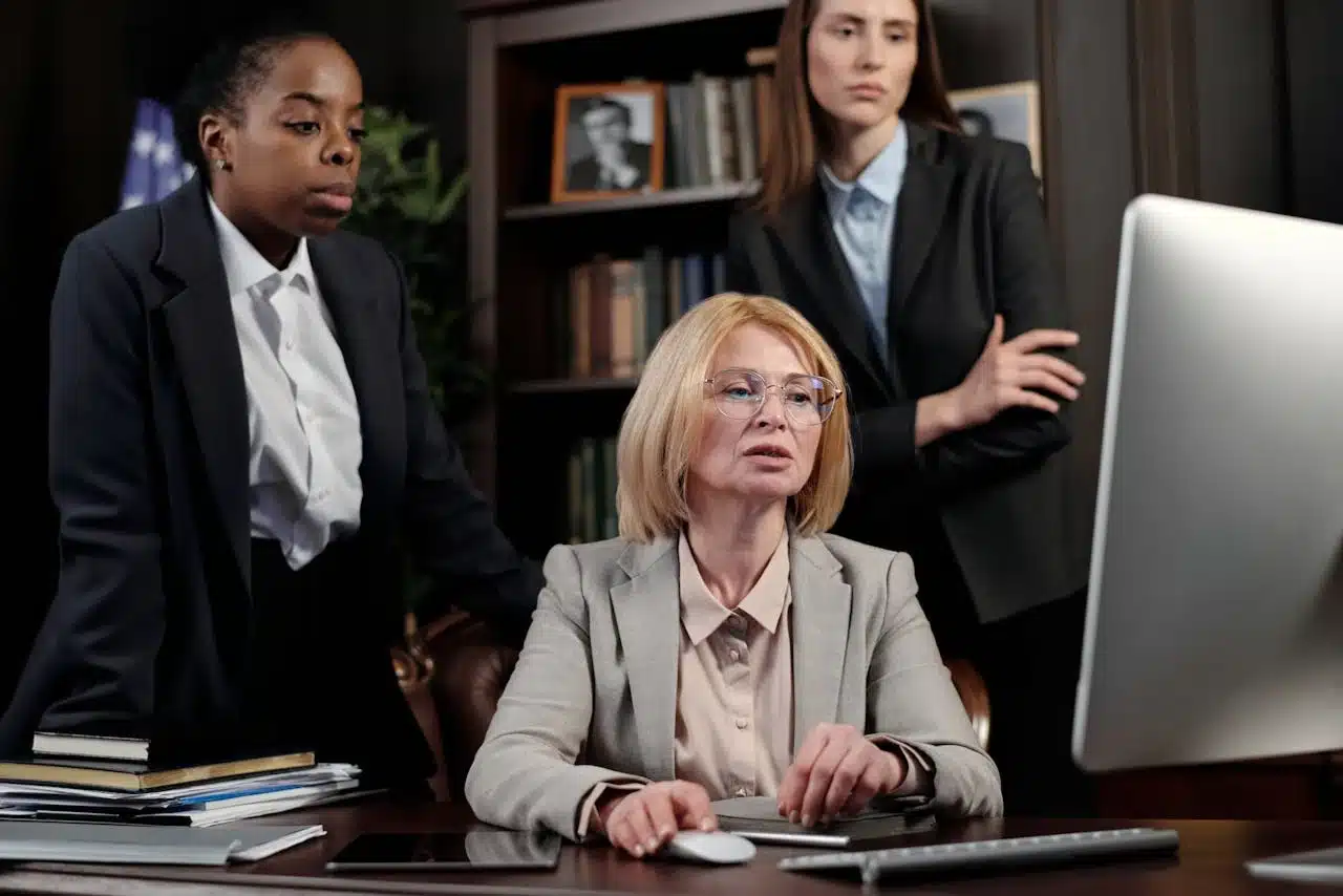 Three women in business attire seated at a desk, engaged in discussion and collaborating on a project.
