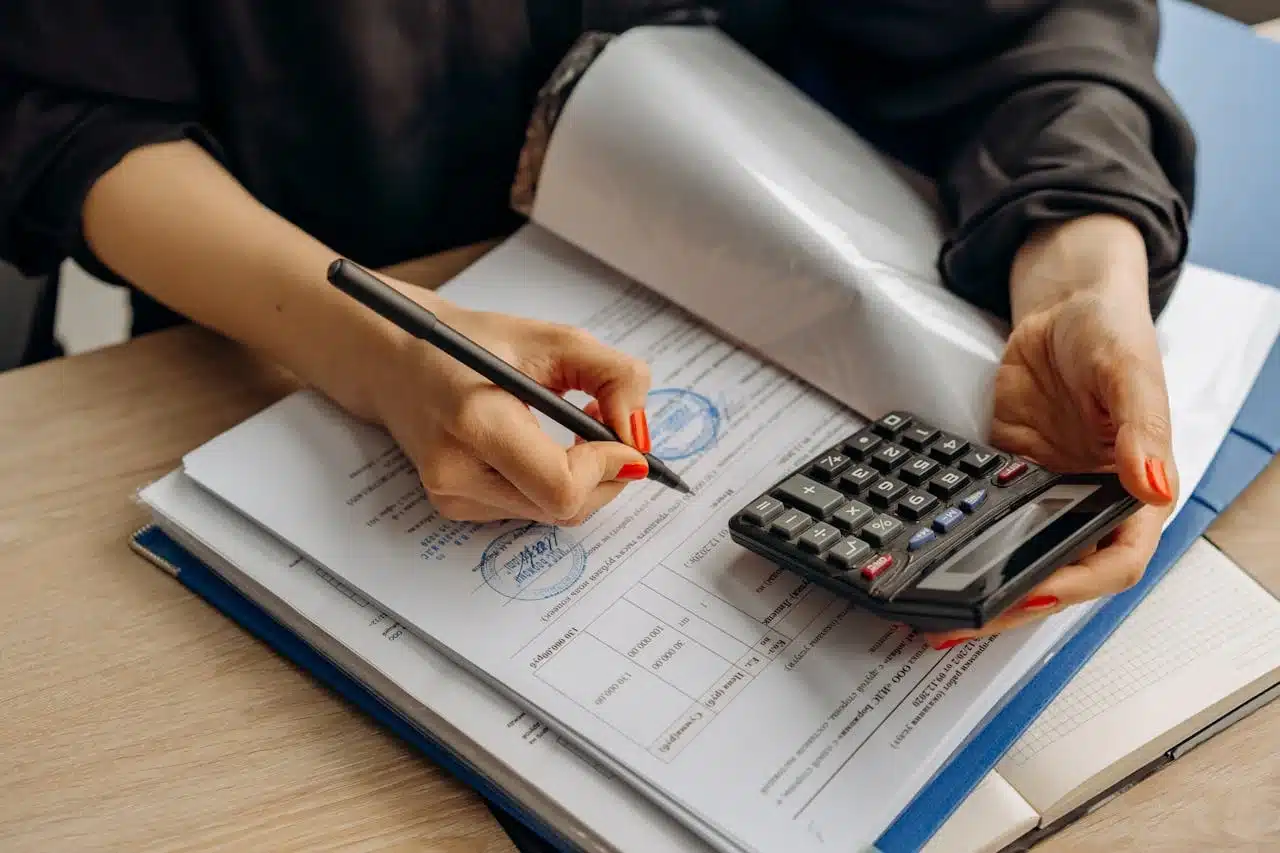 Woman's hands writing on paper while using a calculator, focused on calculations and note-taking
