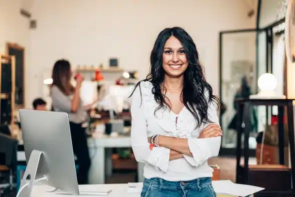 A woman stands confidently in front of a desk, arms crossed, exuding a sense of authority and poise.