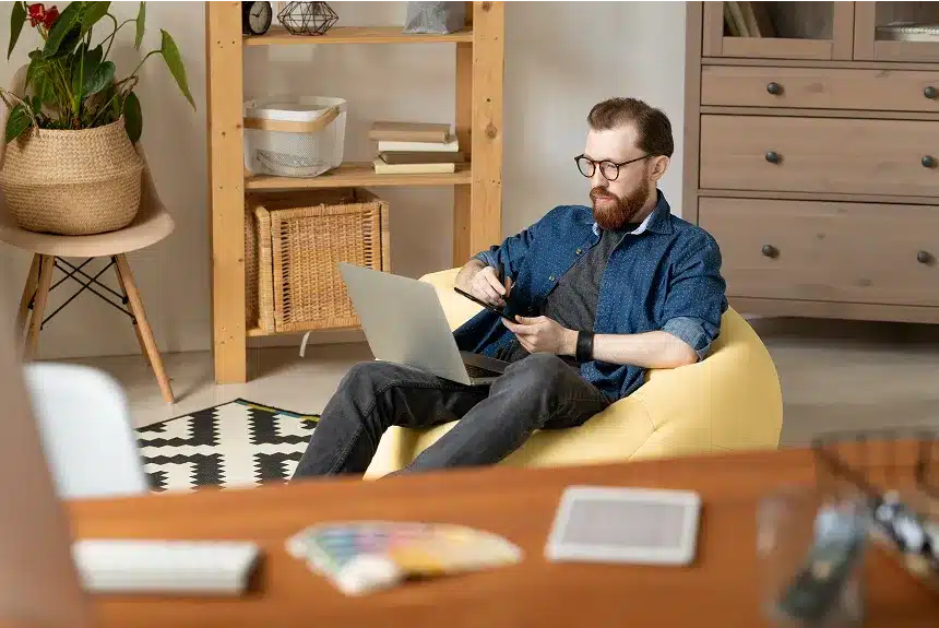 A man sitting comfortably on a bean bag chair, focused on his laptop in a cozy indoor setting.