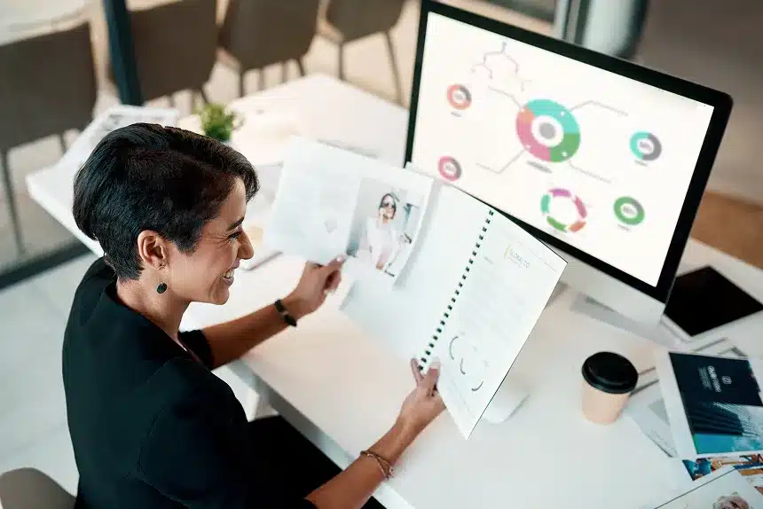 A woman sitting at a desk, focused on her computer screen, with a notepad and pen beside her.