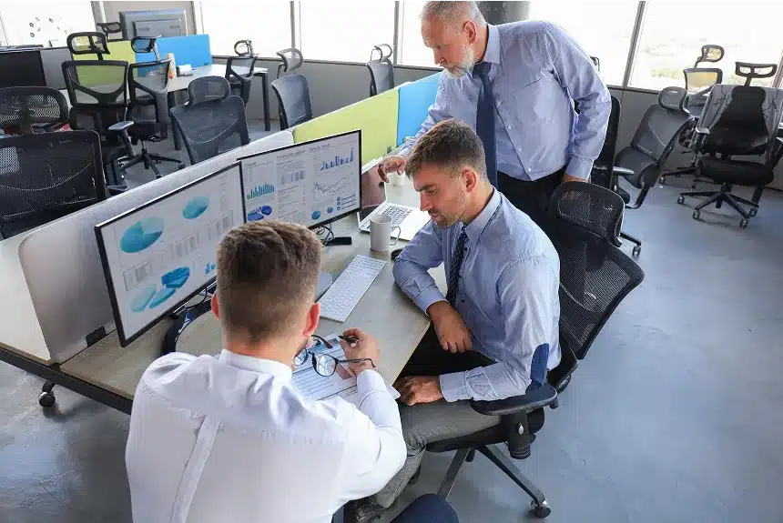 Three men in an office collaborating while looking at a computer screen, engaged in discussion and analysis.