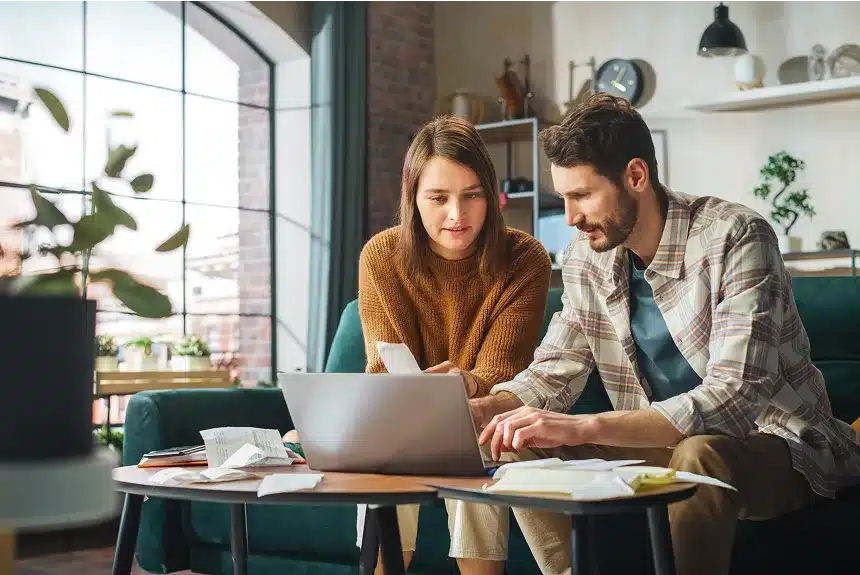 A man and woman sit together on a couch, focused on a laptop in front of them.