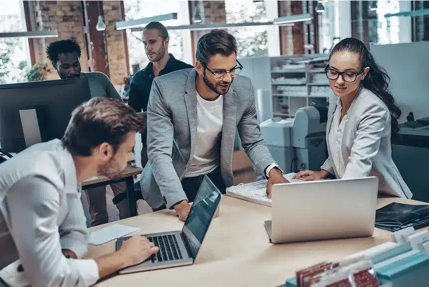 A group of diverse individuals collaborating on a laptop in a modern office setting.