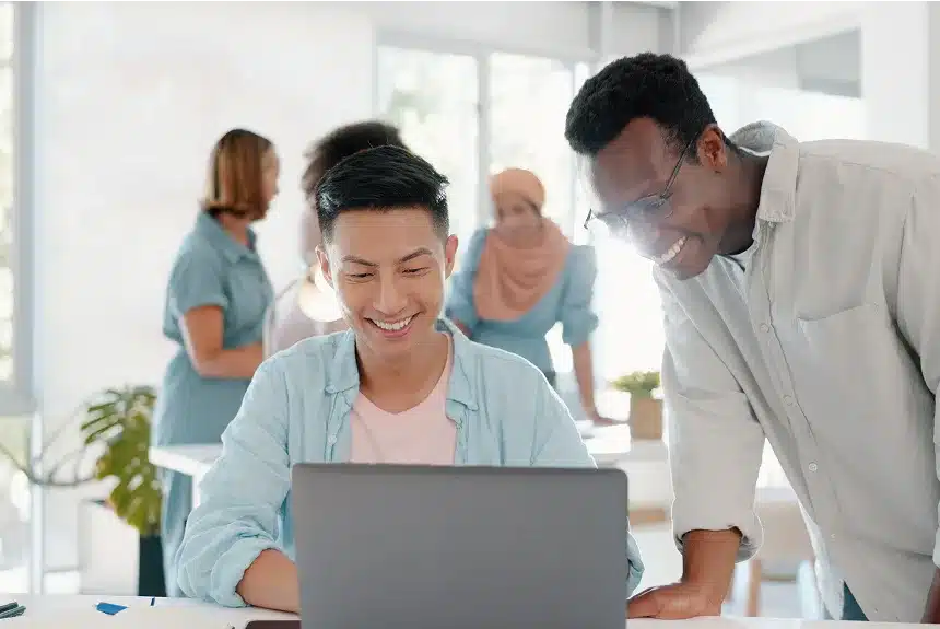 Two men and a woman smile while looking at a laptop, engaged in a friendly discussion or collaboration.