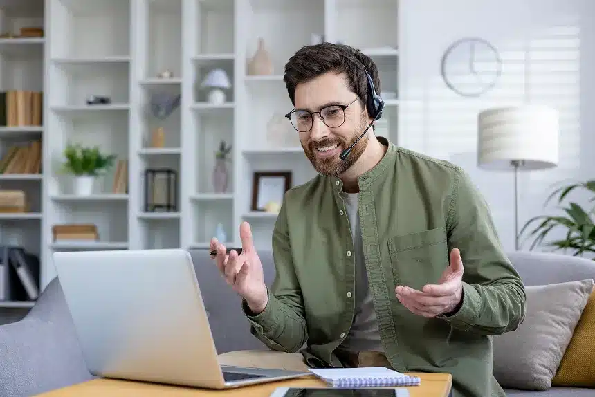 A man with glasses and a headset sits at a laptop, focused on his work in a well-lit environment.
