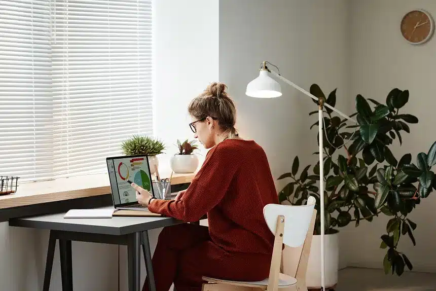 A woman sitting at a desk, focused on her laptop, with a notepad and pen beside her.