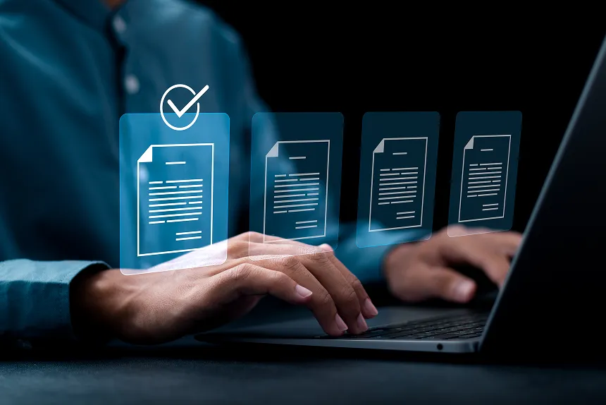 A man focused on a laptop, reviewing documents displayed on the screen in a well-lit workspace.