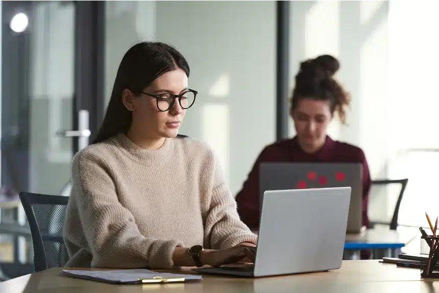 A woman wearing glasses is focused on her work while using a laptop.