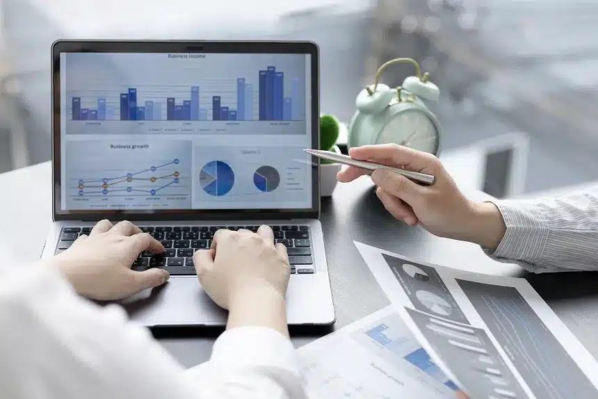 Two individuals collaborating on a laptop displaying various graphs and data analysis.