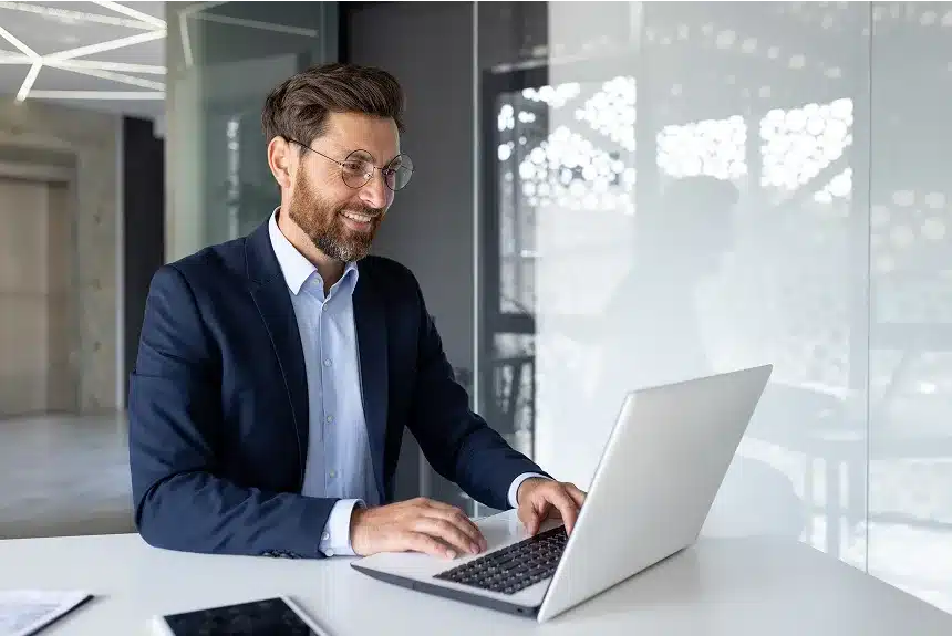 A man in a suit is focused on his laptop, working intently in a professional setting.