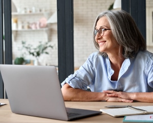 A woman wearing glasses is seated at a table, focused on her laptop while working or studying.