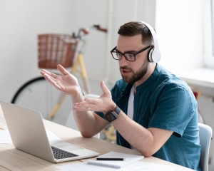 A man with headphones and glasses is seated at a desk, focused on his laptop.