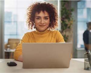 A woman with curly hair is seated at a desk, focused on her laptop, creating a productive work environment.