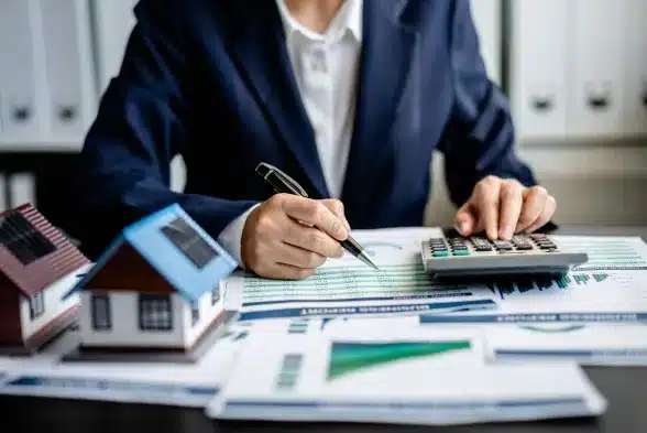 A businesswoman uses a calculator and a house model to assess the value of her property.