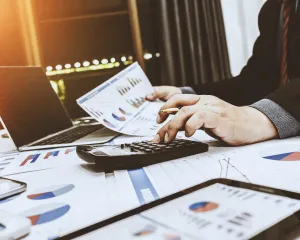 Businessman analyzing financial data with a calculator and laptop, focused on calculations and insights.