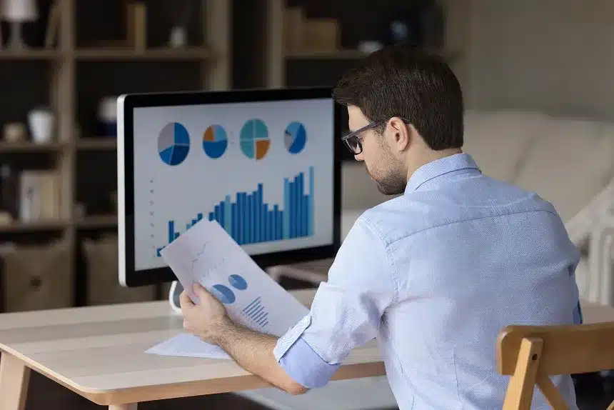 A man sits at a desk, focused on a computer screen displaying various graphs and data visualizations.