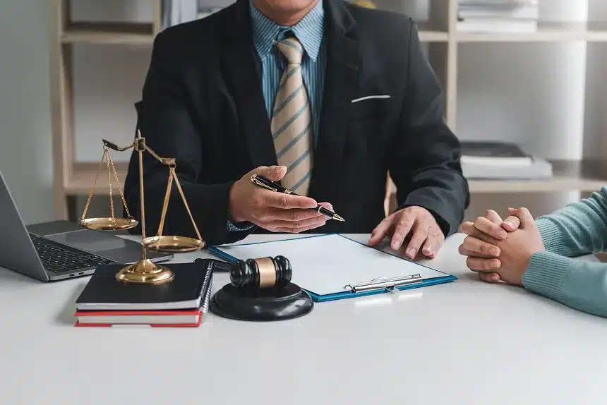 A man in a suit sits at a desk with a laptop and a scale of justice, symbolizing law and legal work.