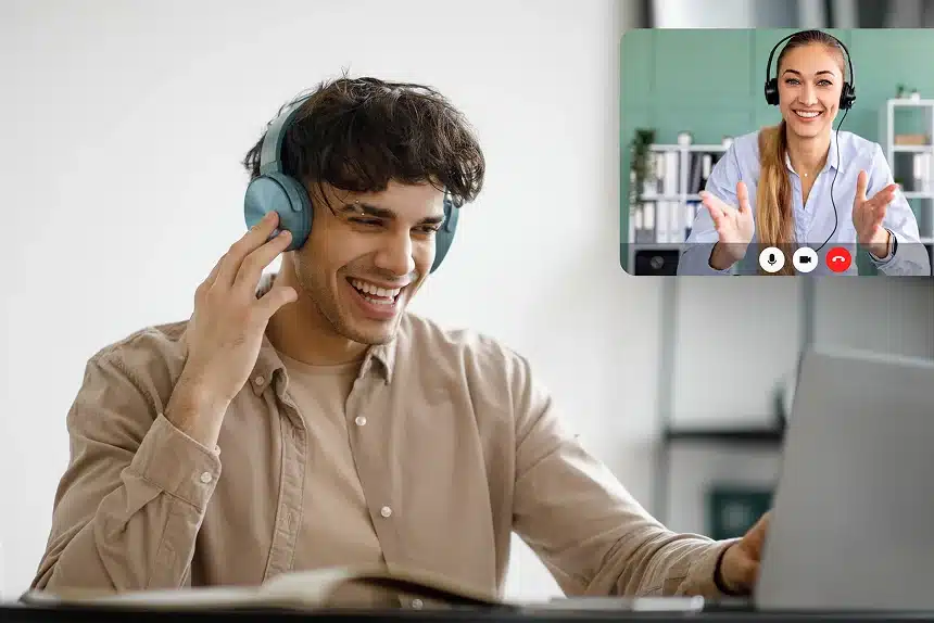 A man with headphones smiles while using a laptop, indicating enjoyment or engagement with his activity.