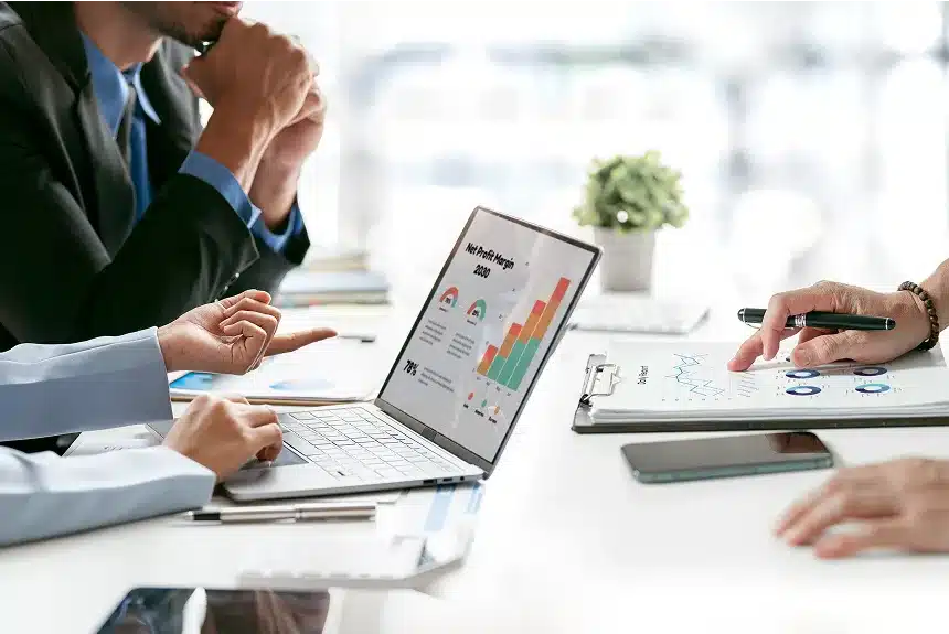 Business professionals seated at a table, collaborating with a laptop and documents spread out before them.