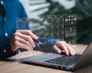 A business professional working on a laptop, viewing a calendar displayed on the screen.