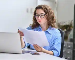 A woman wearing glasses examines a document with a focused expression.