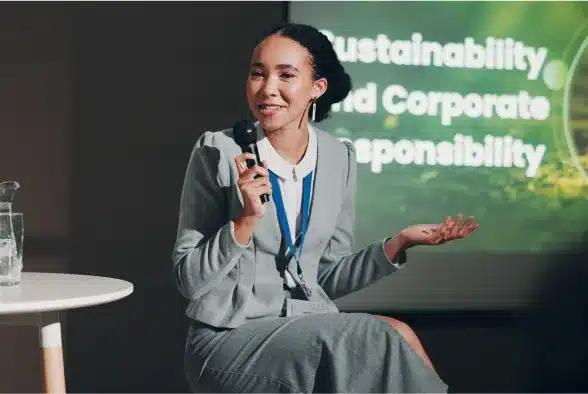 A woman in a business suit delivers a speech at a conference, engaging the audience with her presentation.