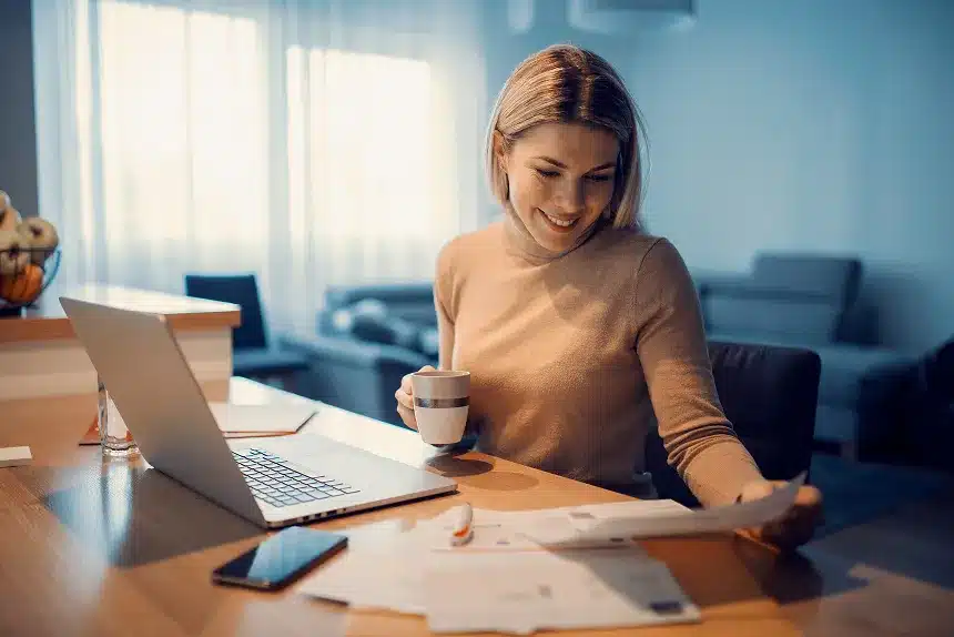 A woman sitting at a table, working on a laptop with a cup of coffee beside her.