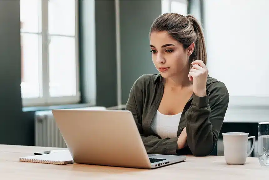 A woman sitting at a table, focused on her laptop, with a calm and organized workspace around her.