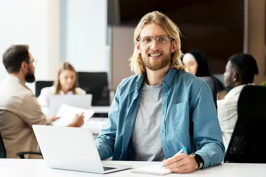 A man with glasses sits at a table, focused on his laptop while working.