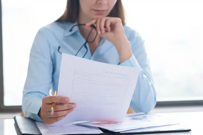 A woman in a blue shirt sits at a desk, focused on a piece of paper in front of her.