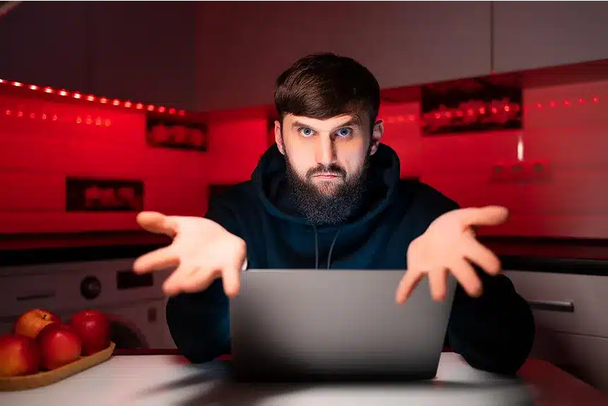 A bearded man working on a laptop while sitting at a kitchen table.