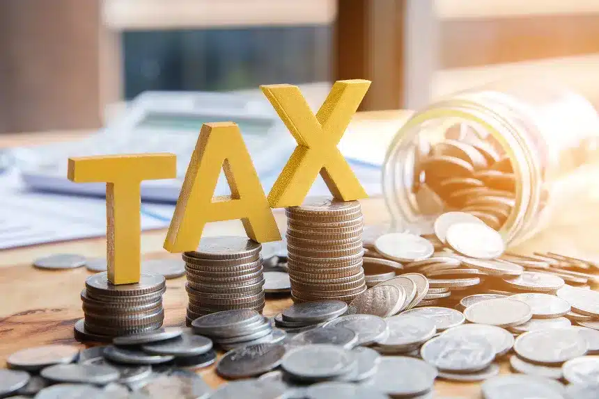 Taxes and money arranged on a wooden table, featuring a prominent tax sign in the background.